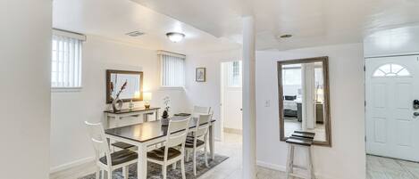 A dining area with a table, chairs, and a rug. There is a mirror on the wall and a door in the background.