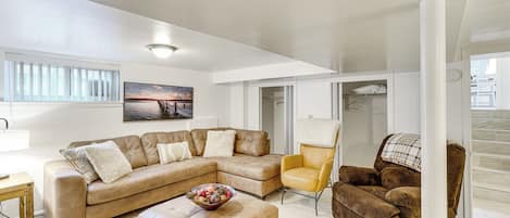 A living room with a sectional sofa, a yellow armchair, a brown armchair, a wooden side table, and a bowl of fruit.