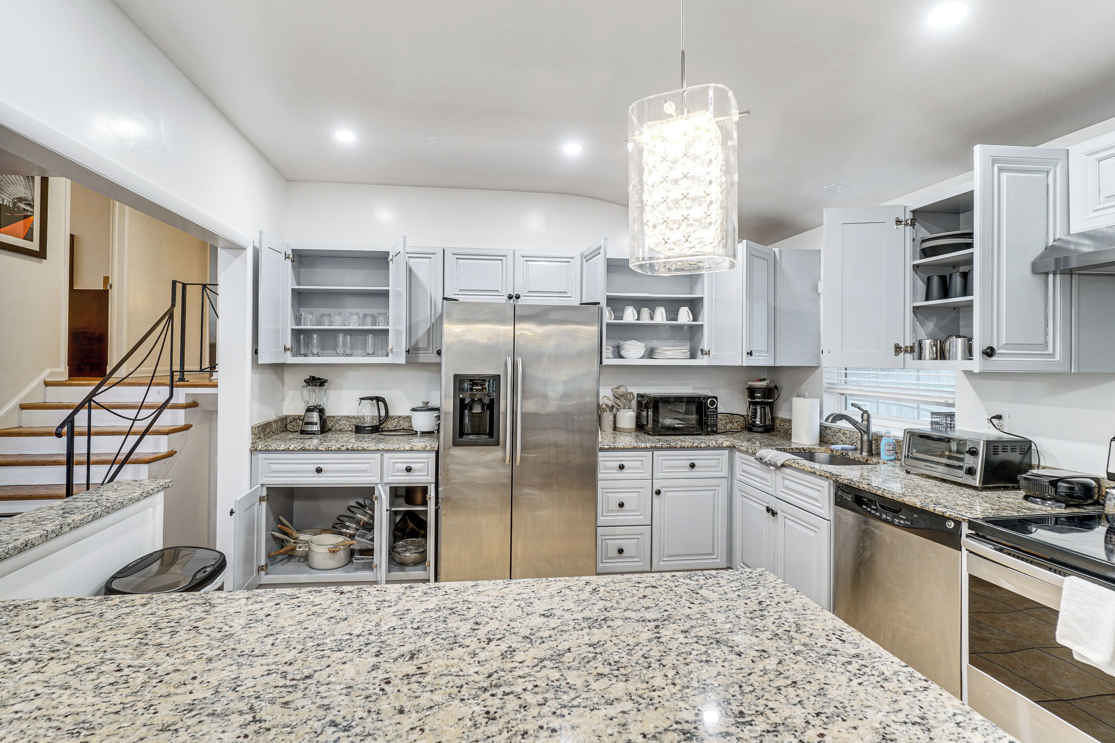A modern kitchen with granite countertops, white cabinetry, a stainless steel refrigerator, a microwave, and a dishwasher.