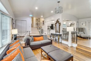 A spacious living room with a grey sofa, ottoman, and a staircase leading to a kitchen. - Group Getaway! Modern Silver Spring Home w/ Yard (Silver Spring)