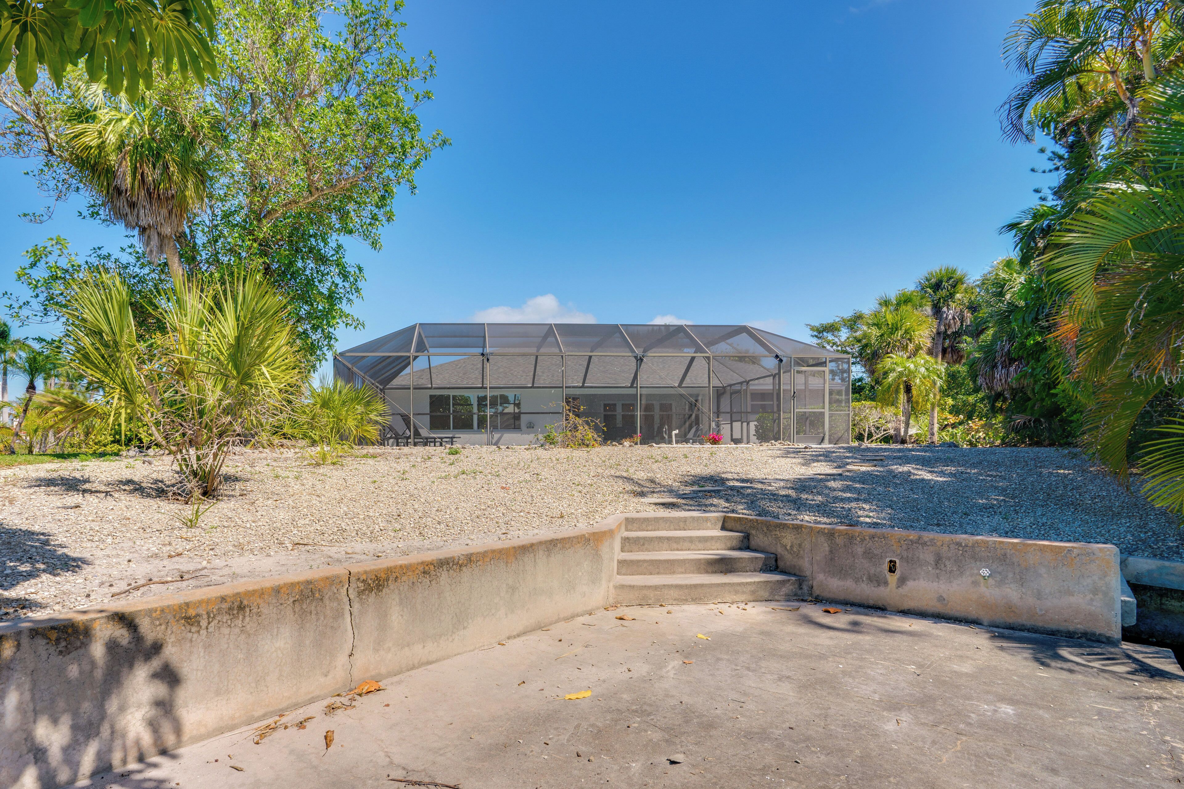 A greenhouse structure with a clear roof, surrounded by gravel and palm trees.