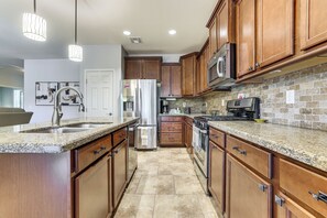 A kitchen with wooden cabinets, granite countertops, stainless steel appliances, and pendant lighting. - Luxe 55-plus Retreat 4 Mi to Golf Club of Estrella (Goodyear)