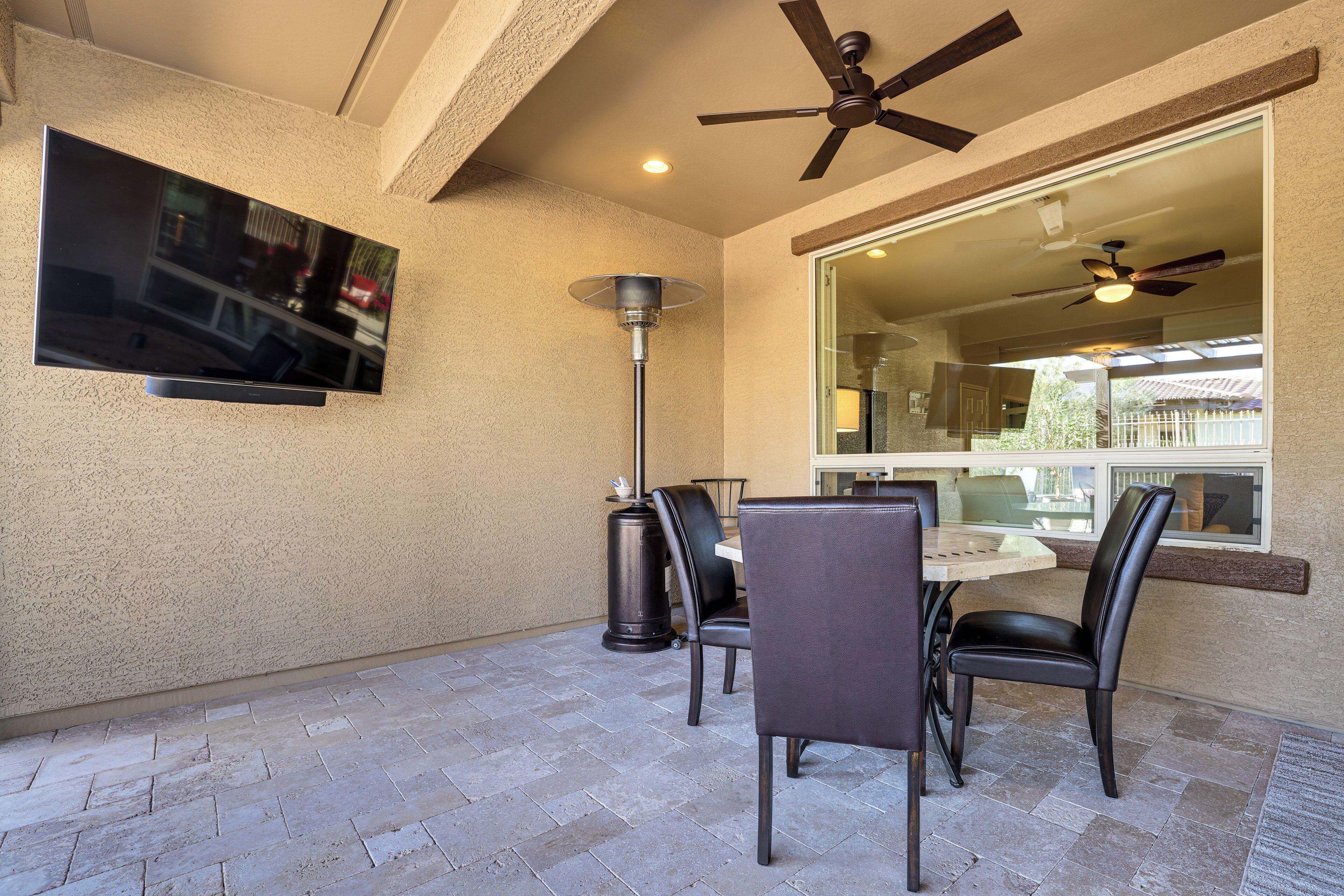 A patio with a dining table, chairs, ceiling fans, and a TV mounted on the wall.
