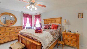 Een slaapkamer met een houten bed, een plafondventilator, een dressoir, een nachtkastje en een spiegel.