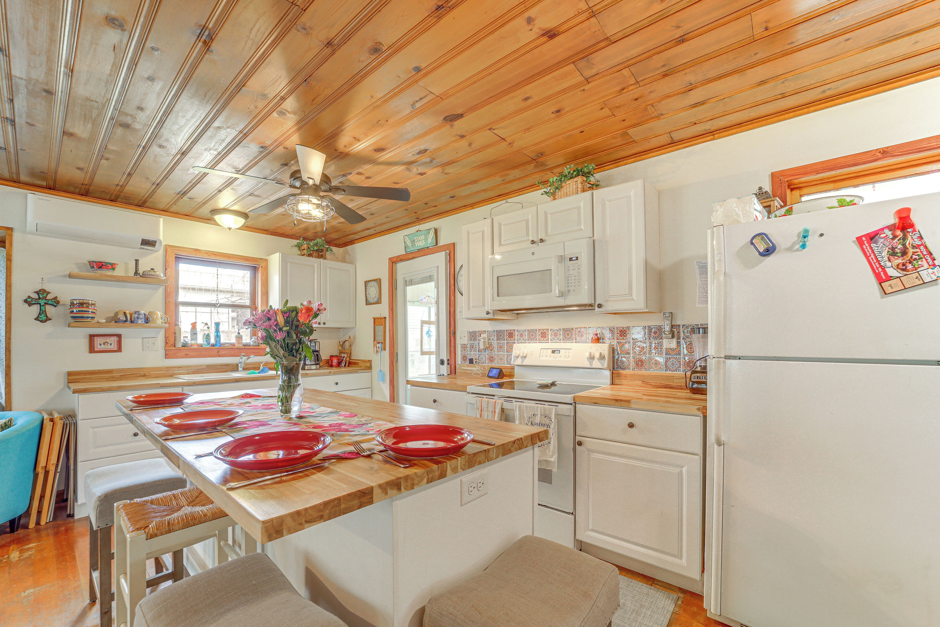 Une cuisine avec un plafond en bois, des armoires blanches, un îlot central avec des assiettes rouges et un réfrigérateur décoré d’aimants.