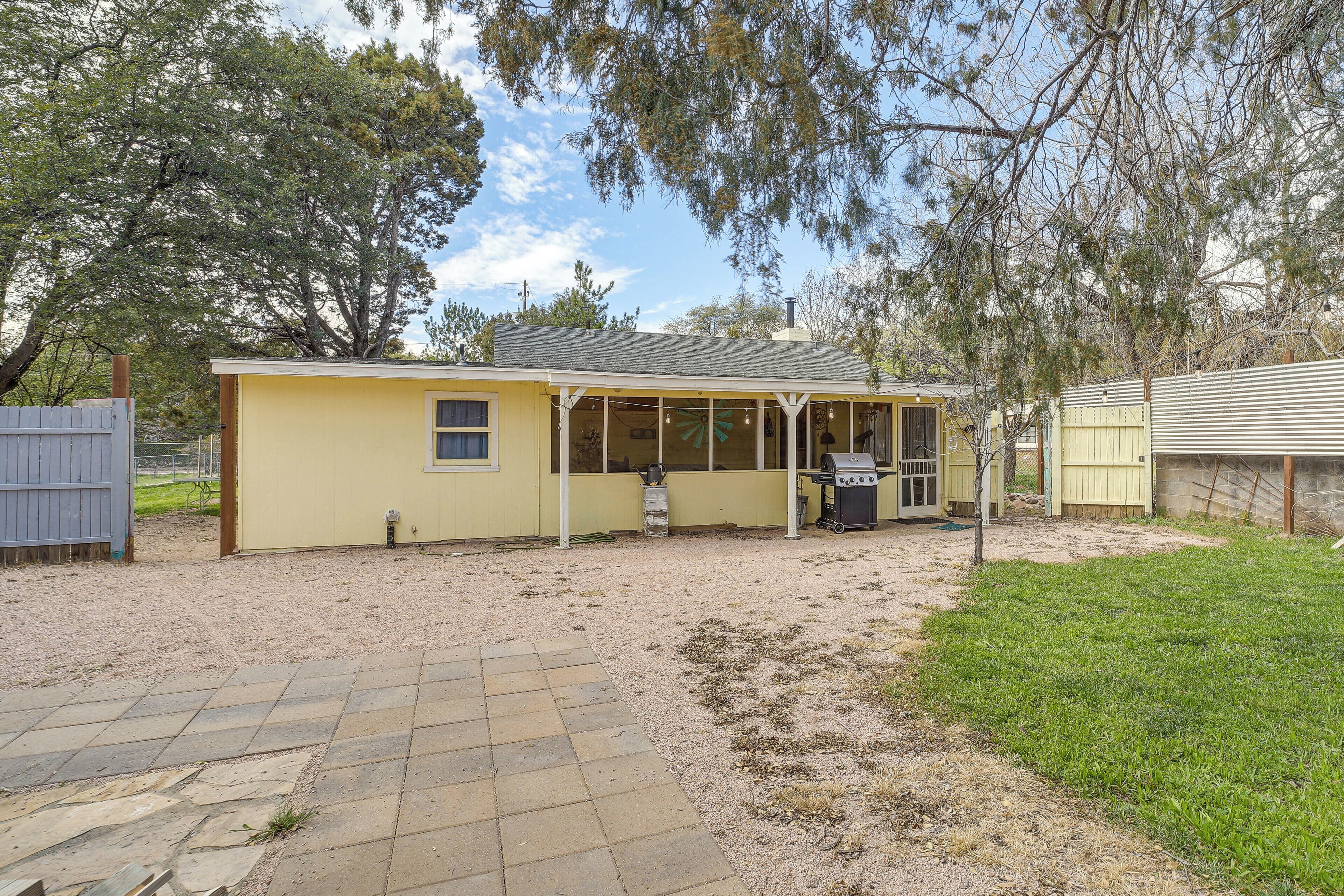 A single-story yellow building with a covered patio area, a grill, and a fenced yard.
