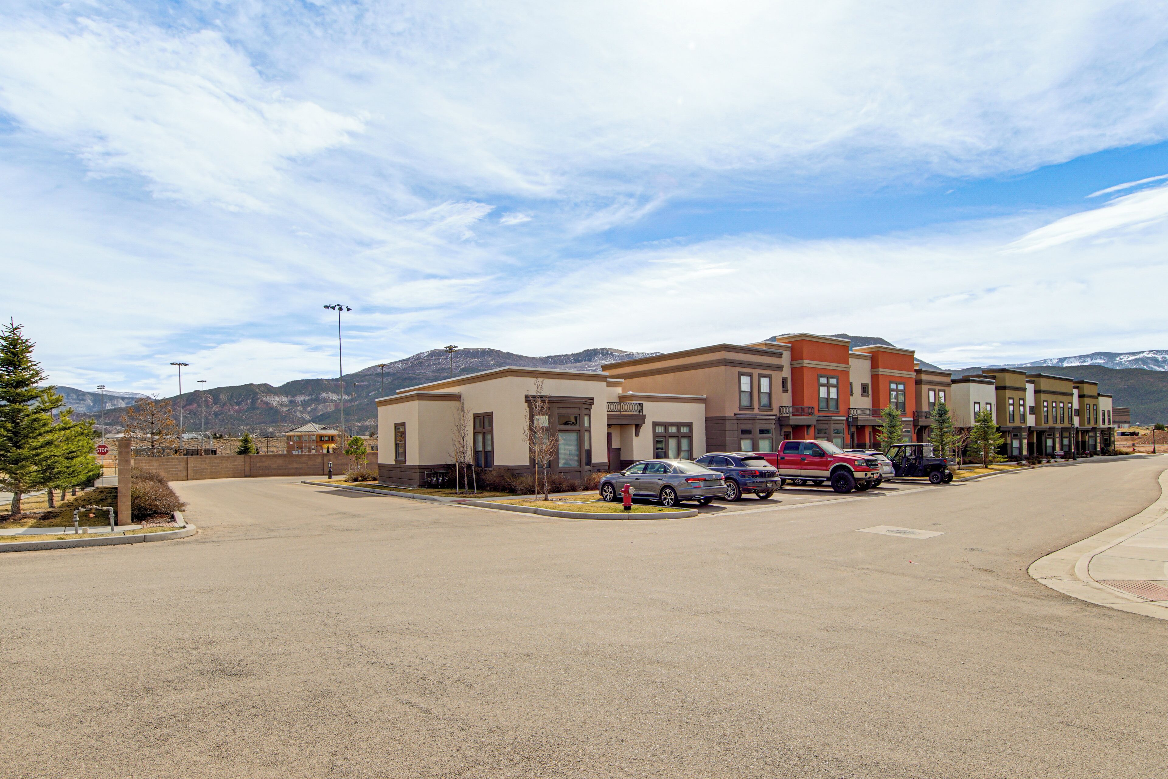 A parking lot with several cars, a building with multiple stories, and mountains in the background.