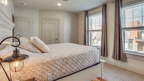 Une chambre à coucher avec un lit, un ventilateur de plafond, une fenêtre avec des rideaux et une vue sur les bâtiments à l’extérieur.