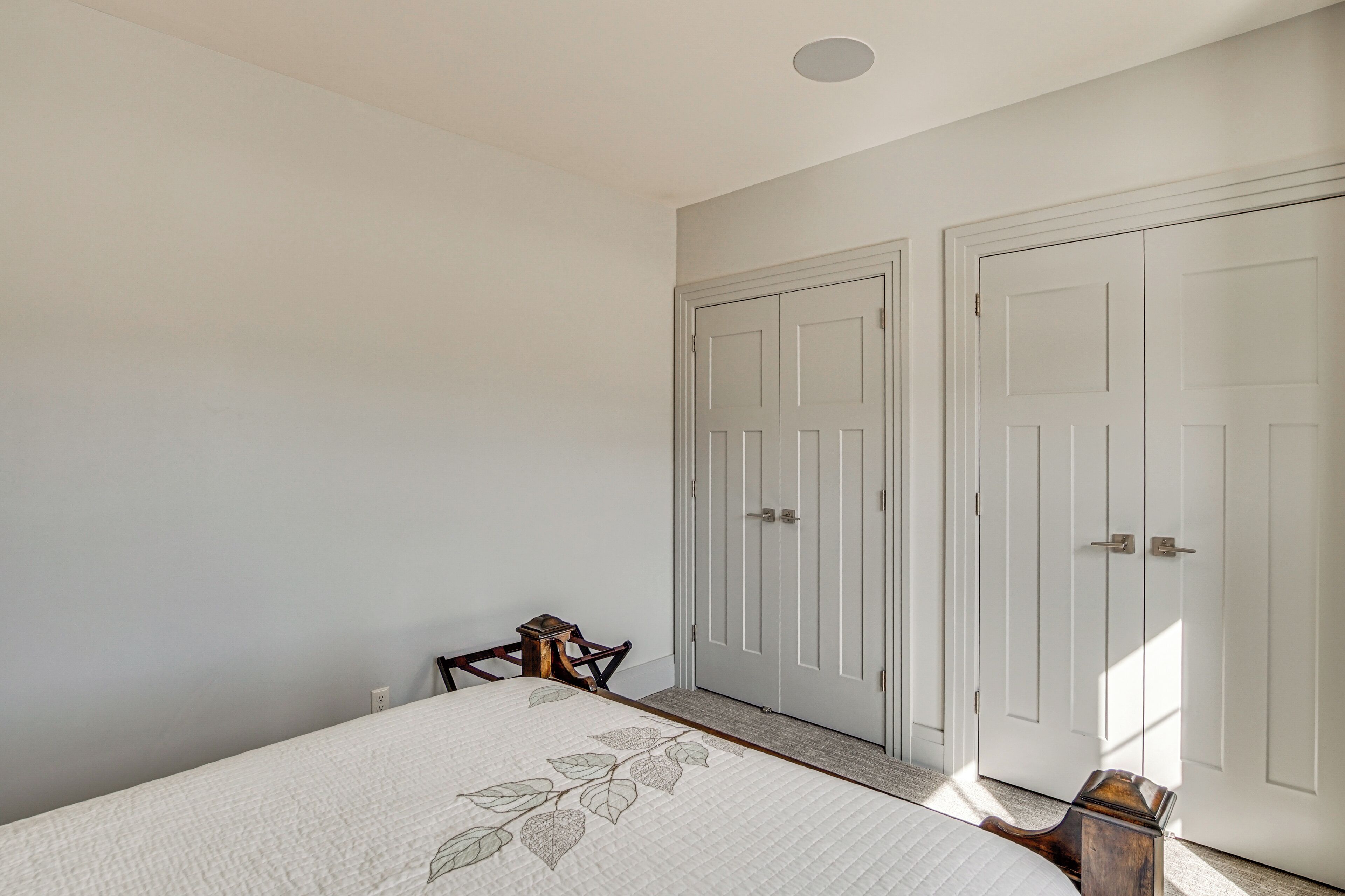 A bedroom with a bed, two white doors, a small wooden chair, and a nightstand.