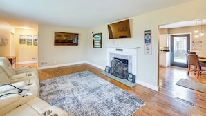 Een woonkamer met een open haard, een bank, een vloerkleed en een eethoek.