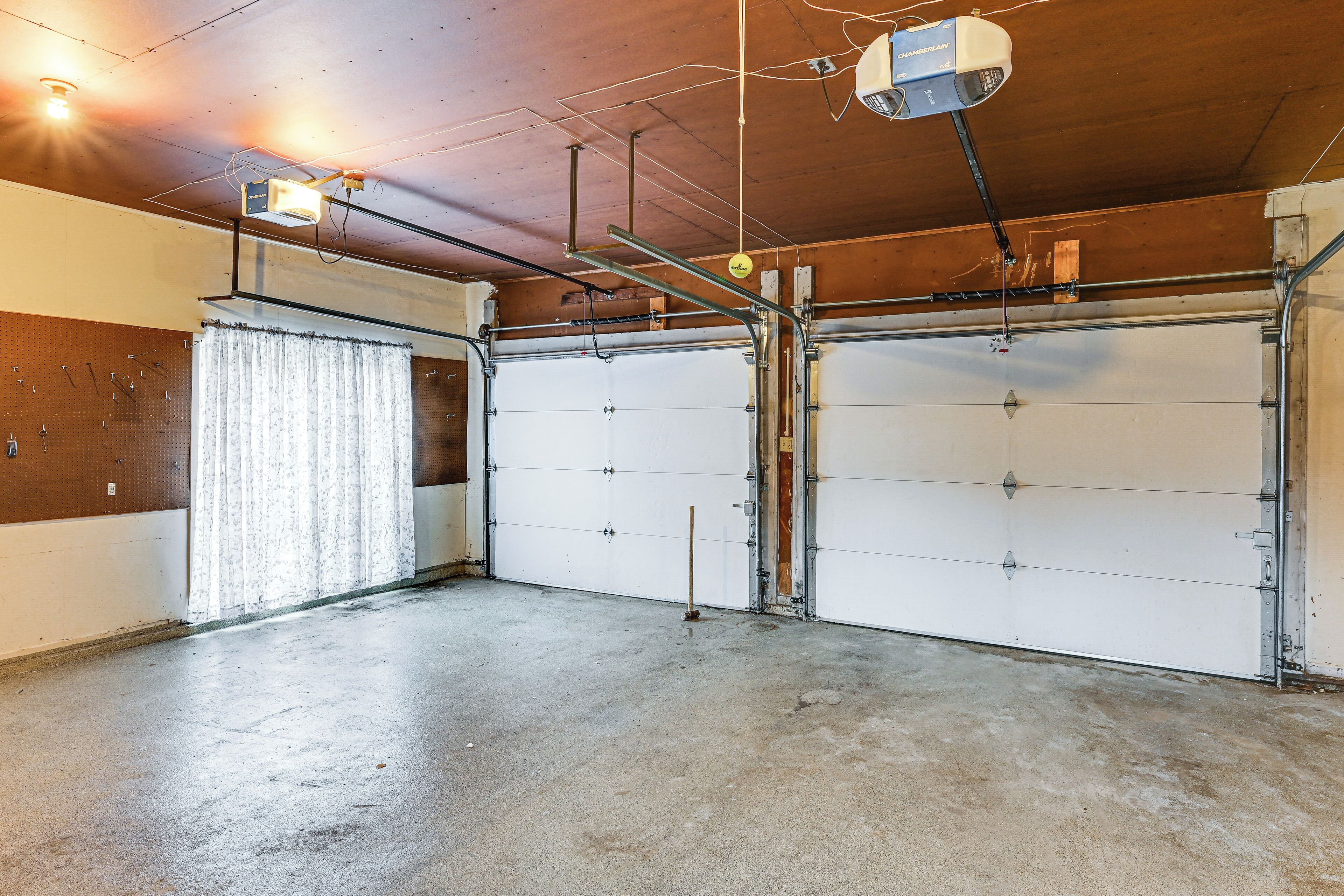 A garage with two white garage doors, a concrete floor, and exposed ceiling wiring.