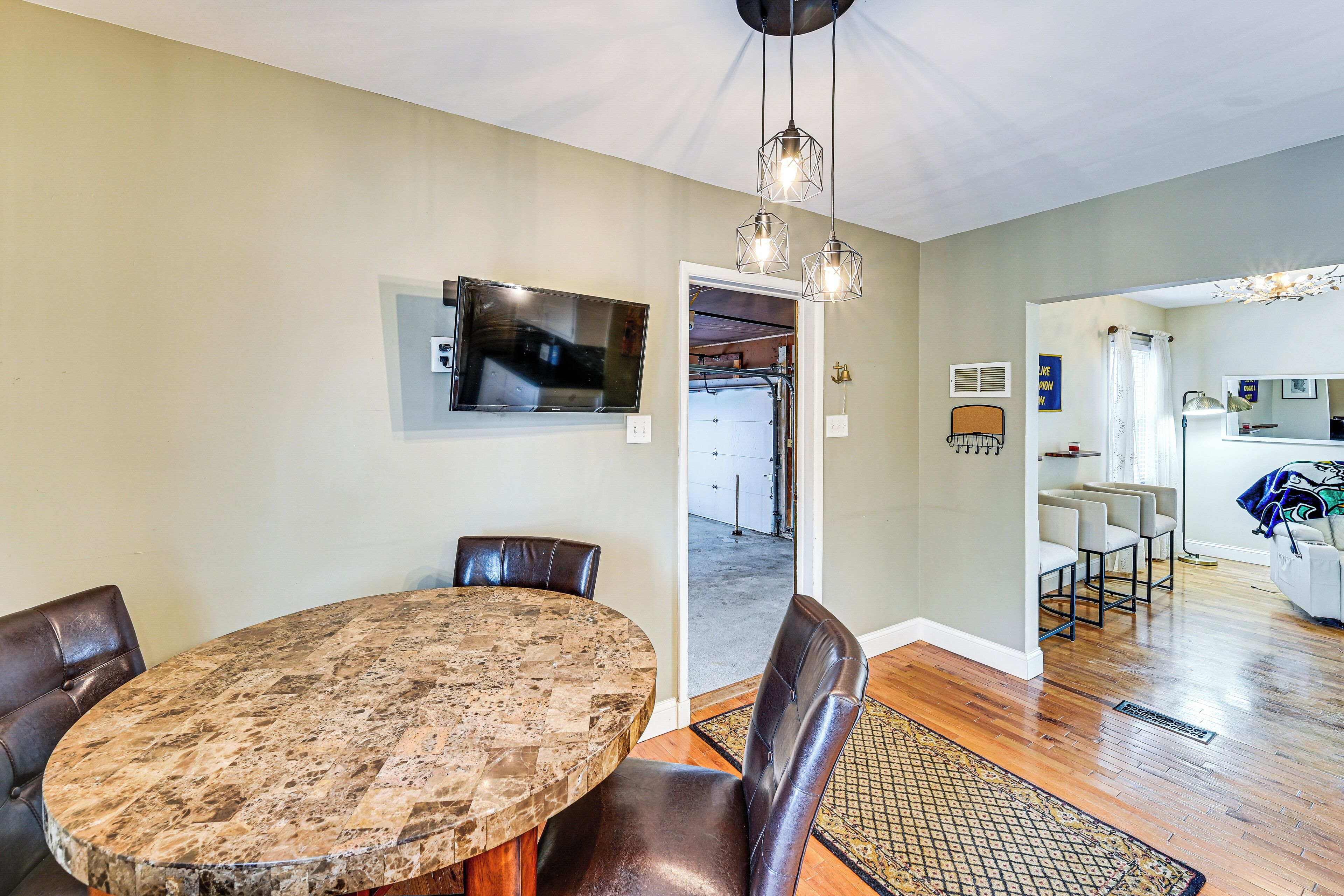 A dining area with a round table, chairs, a television, and a kitchen visible in the background.