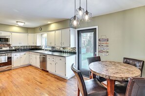 A modern kitchen with white cabinets, a wooden floor, a dining area with a round table and chairs, and pendant lights. - South Bend Home: 2 Mi to Notre Dame & Stadium (South Bend)