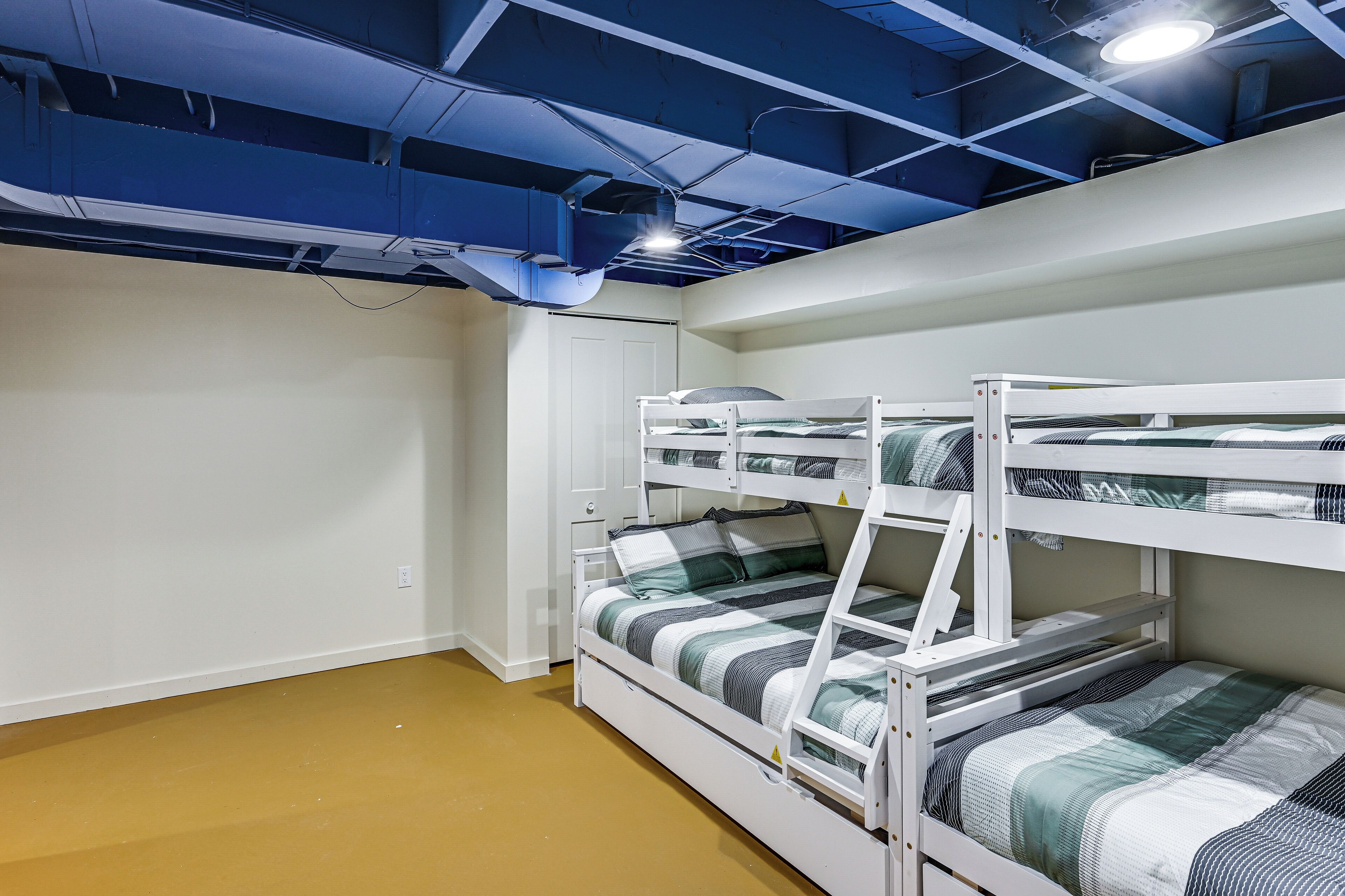 A bunk bed room with a white door, a brown floor, and a blue ceiling with exposed pipes.