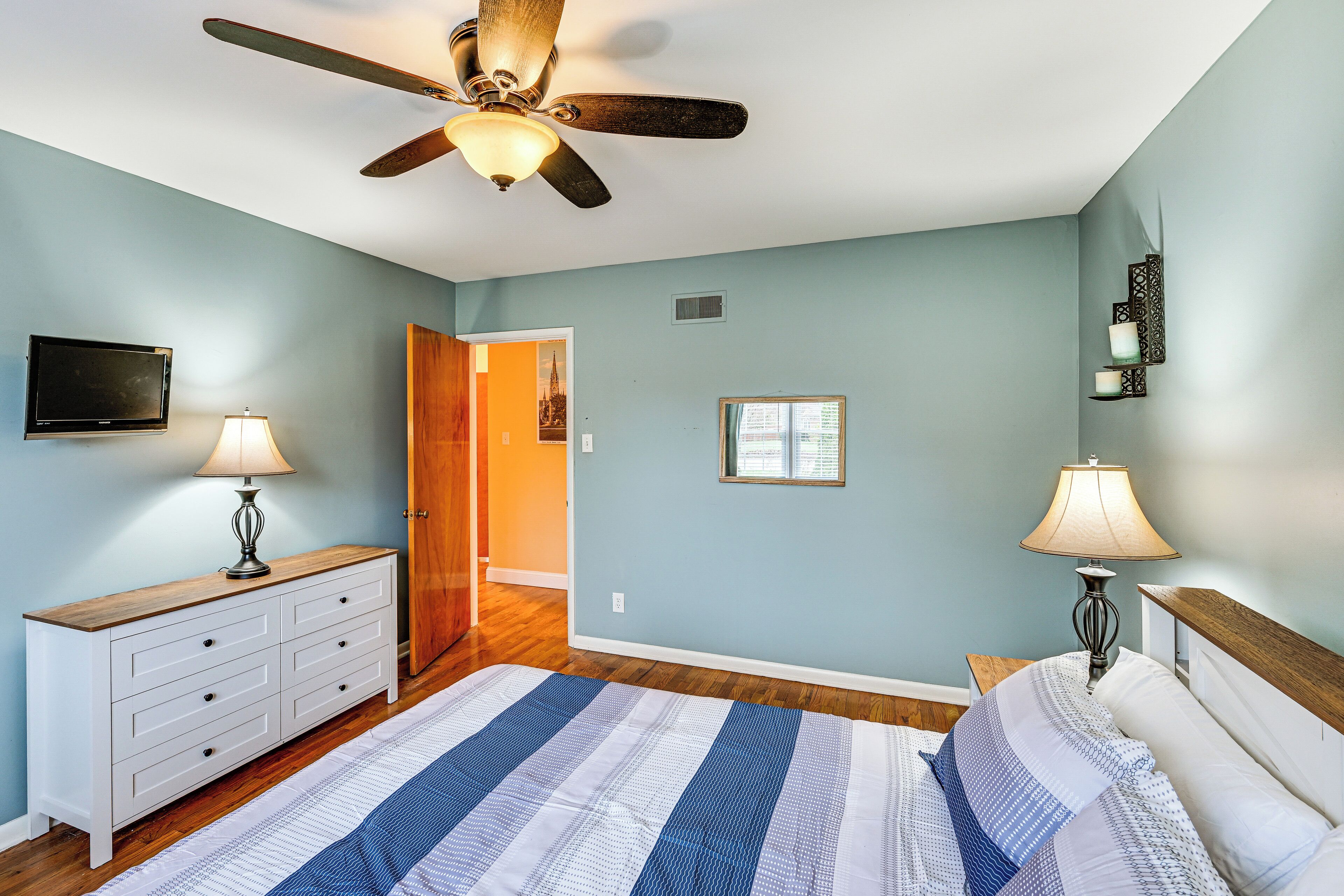 A bedroom with a bed, a ceiling fan, a dresser, a nightstand, a lamp, and a television.