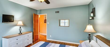 A bedroom with a bed, a ceiling fan, a dresser, a nightstand, a lamp, and a television.