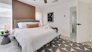 Ein modernes Schlafzimmer mit einem Bett, einem Deckenventilator und einem gemusterten Teppich.