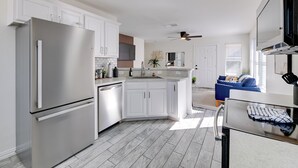 Eine moderne Küche mit weißen Schränken, einem Edelstahl-Kühlschrank, einem eingebauten Backofen und einem Deckenventilator.