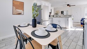 Eine moderne Küche mit weißen Schränken, ein Essbereich mit Tisch für zwei Personen und einem Deckenventilator.