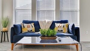 Ein Wohnzimmer mit einem blauen Sofa, einem Glastisch und einer Zimmerpflanze.