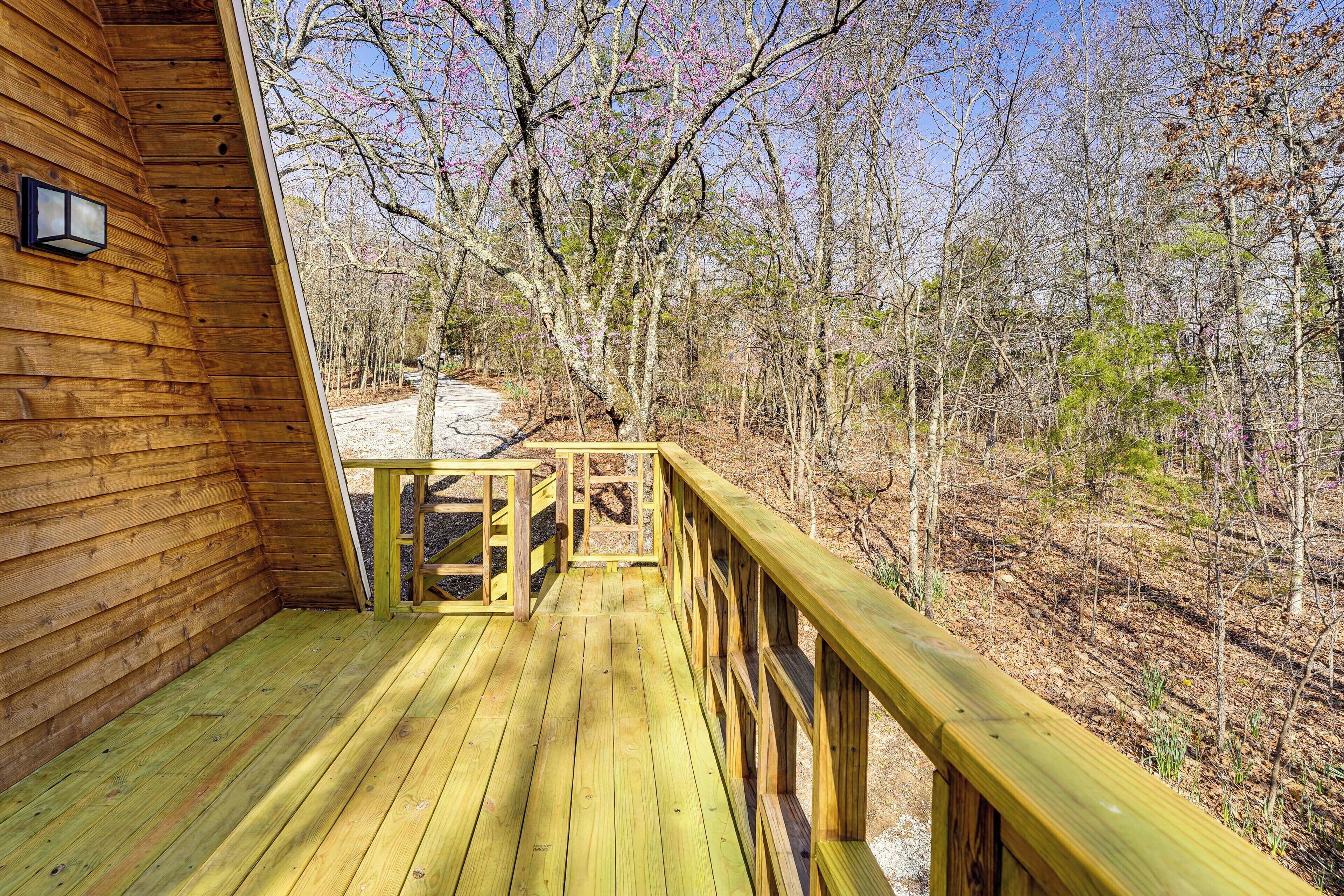 A wooden deck with a railing, surrounded by trees and a clear sky.