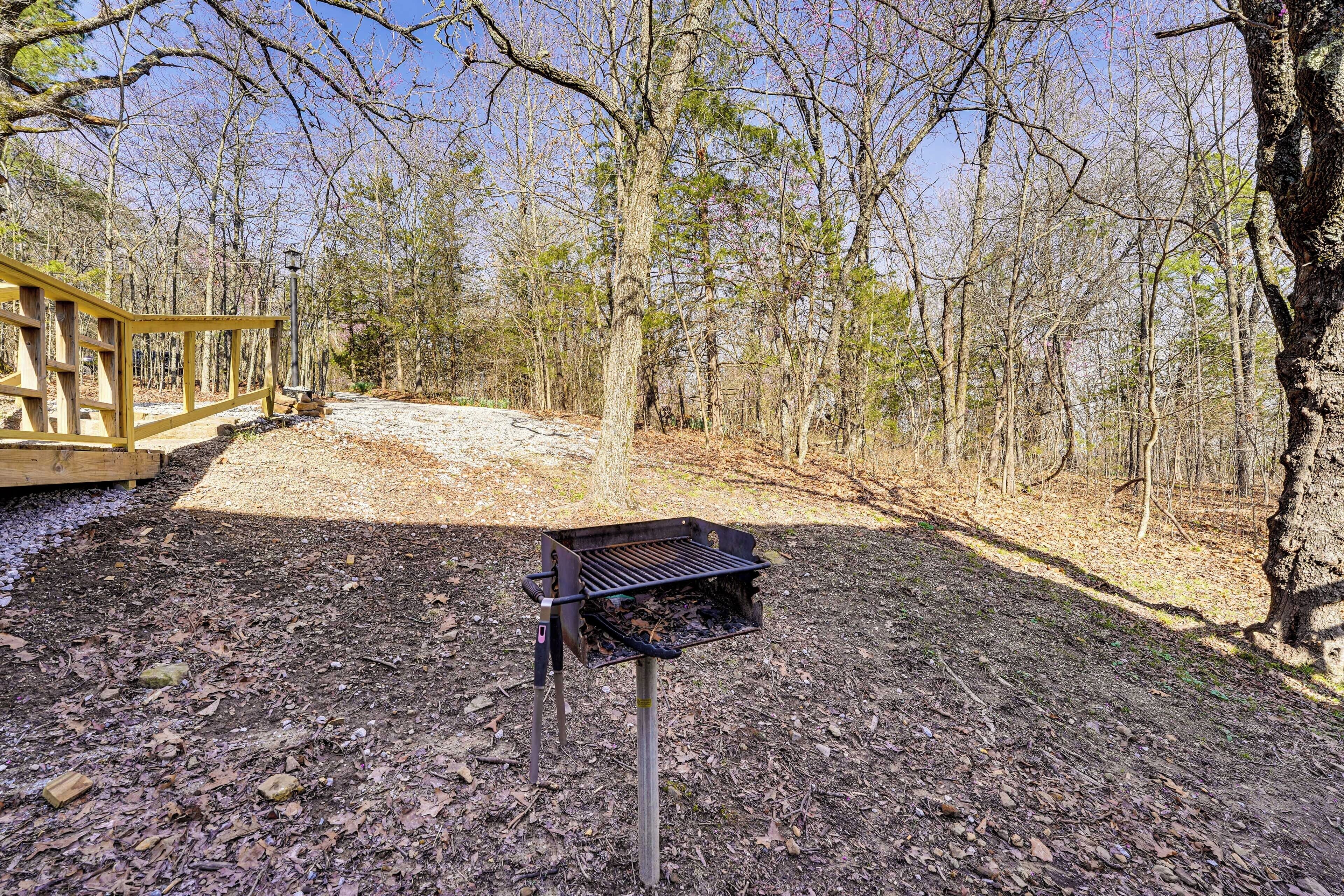 A grill in a wooded area with a wooden deck and trees in the background.