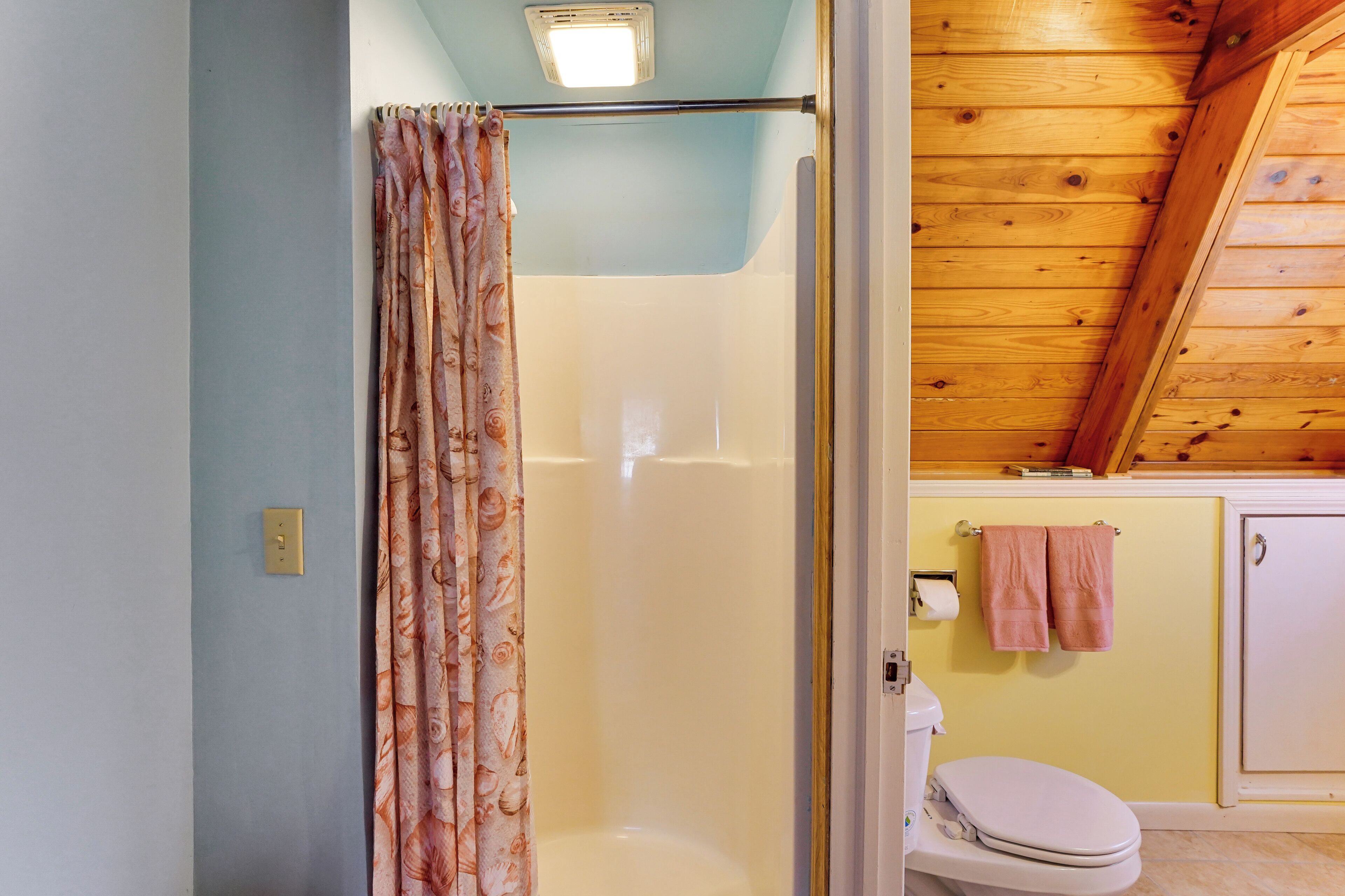 A bathroom with a shower, toilet, and wooden ceiling.
