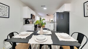 Un coin repas avec une table noire, des sets de table blancs et un vase rempli de fleurs.