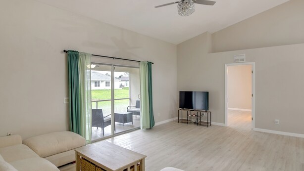 A spacious living room with a sofa set, a television, and a sliding glass door leading to an outdoor area. - Lehigh Peace Retreat Near Ft Myers! Pet-friendly (Lehigh Acres)