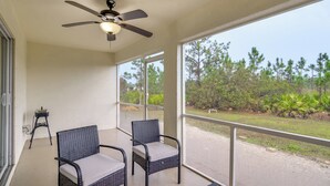 A balcony with two wicker chairs, a ceiling fan, and a view of a road and trees. - Lehigh Peace Retreat Near Ft Myers! Pet-friendly (Lehigh Acres)