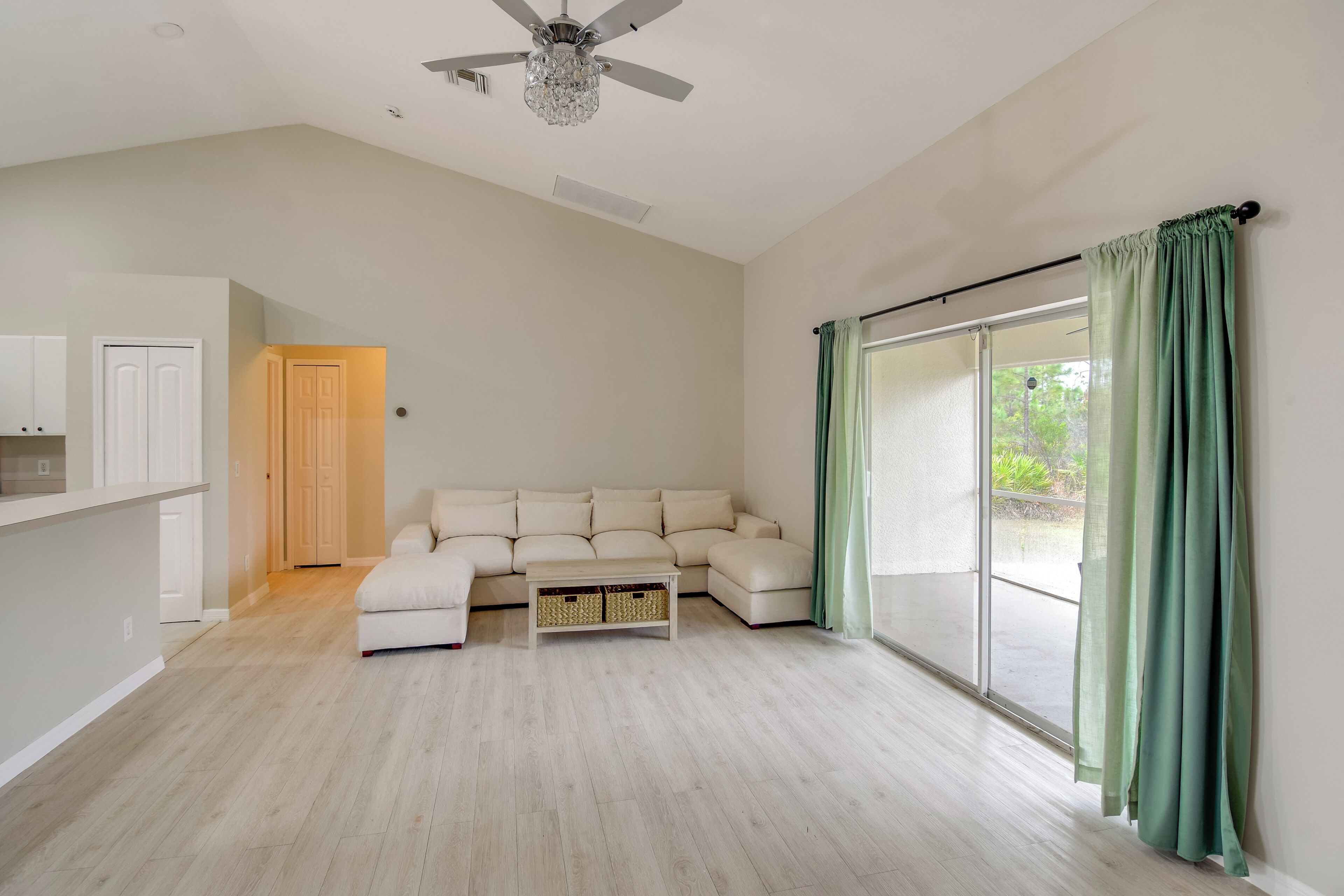Amplia sala de estar con un sofá seccional grande, ventilador de techo y puerta corredera de vidrio con cortinas.