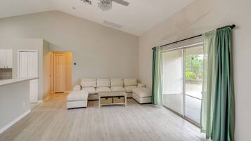 Amplia sala de estar con un sofá seccional grande, ventilador de techo y puerta corredera de vidrio con cortinas.