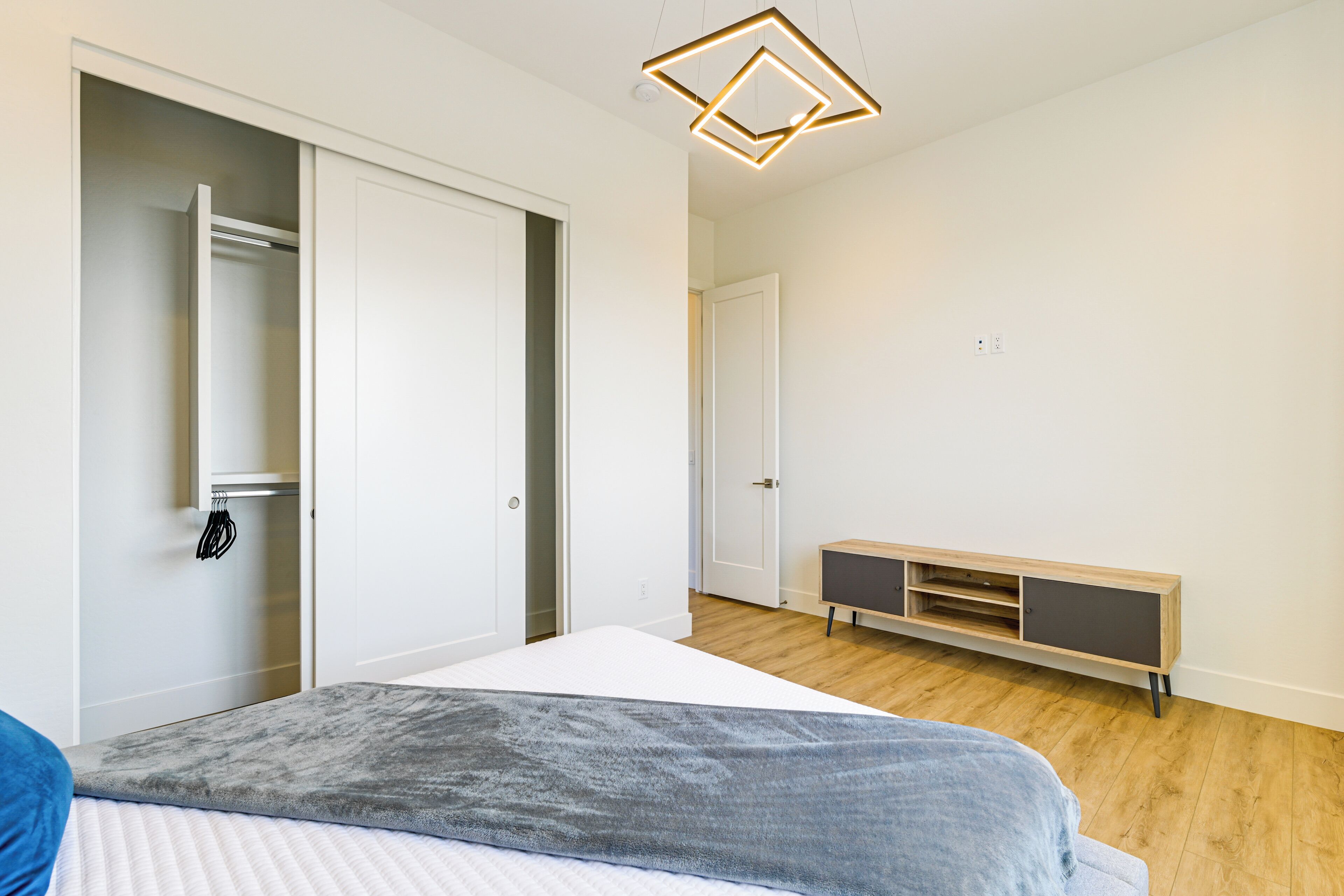 Un dormitorio con cama, armario, mueble empotrado para la televisión y una lámpara colgante.