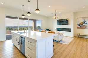 A modern kitchen with a large island, pendant lighting, and a view of the outdoors.