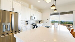 A modern kitchen with stainless steel appliances, white cabinetry, and a large island. - Gateway to Route 66 Fun! Mtn-view Williams Home (Williams)