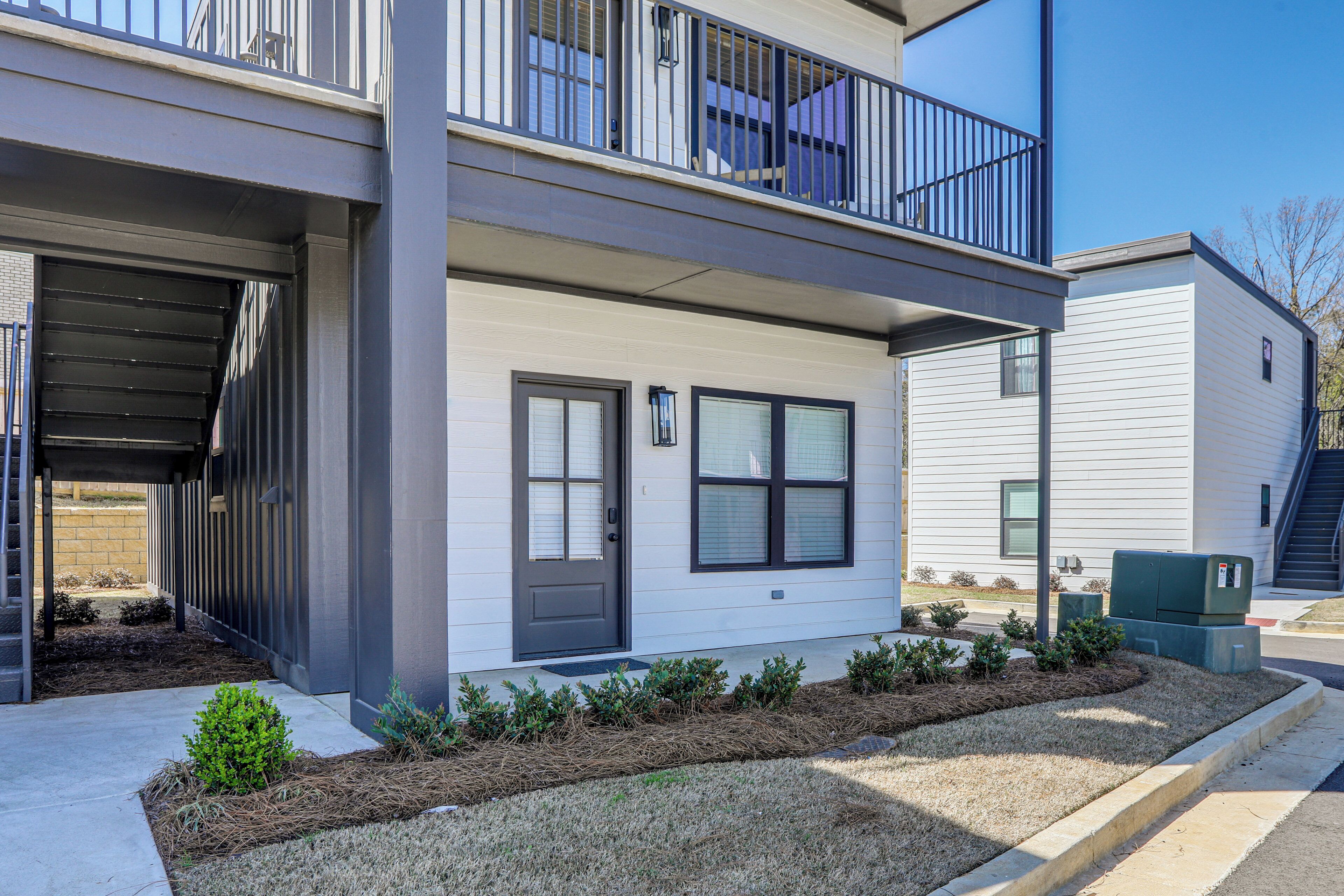 A two-story residential building with a covered entryway, a balcony, and a small front yard with landscaping.
