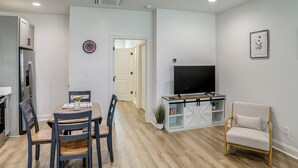 A modern kitchen with a built-in refrigerator, a dining table with chairs, a TV on a stand, and a seating area with a chair.