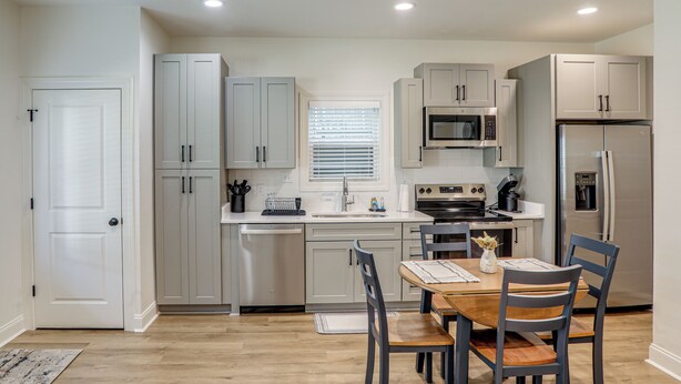 A modern kitchen with white cabinets, a dining table with chairs, and a refrigerator.