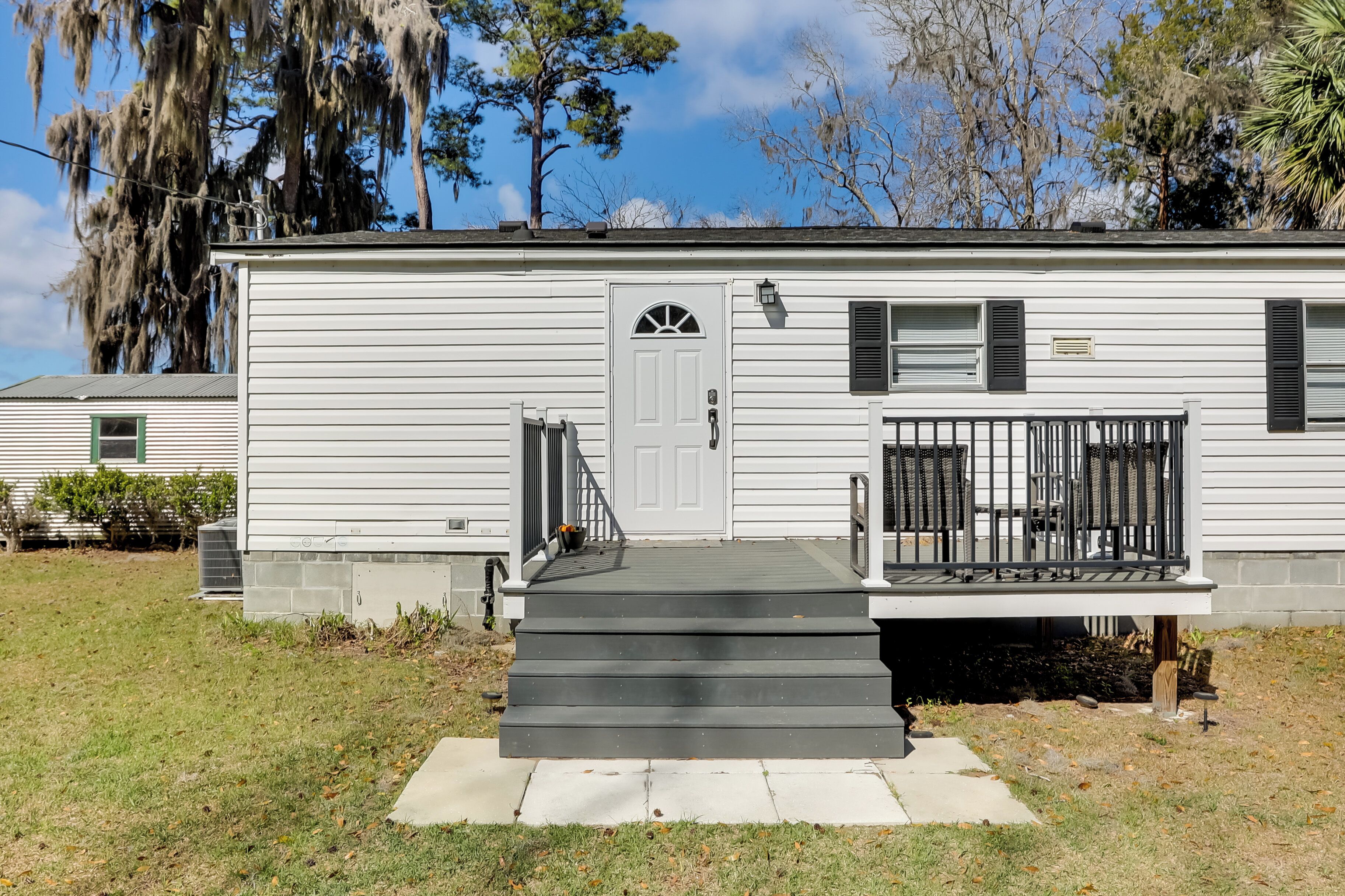 A single-story mobile home with a front porch, a door with a window, and a small front yard.