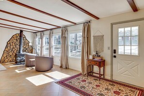 A room with a stone fireplace, large windows, a door with a geometric design, and a patterned rug. - Private Boat Dock at Waterfront Lake Mitchell Home (Cadillac)