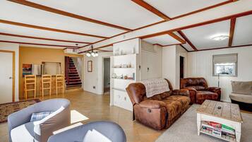 A spacious living area with a dining area, a brown leather sofa, a coffee table, and a staircase leading to another level.