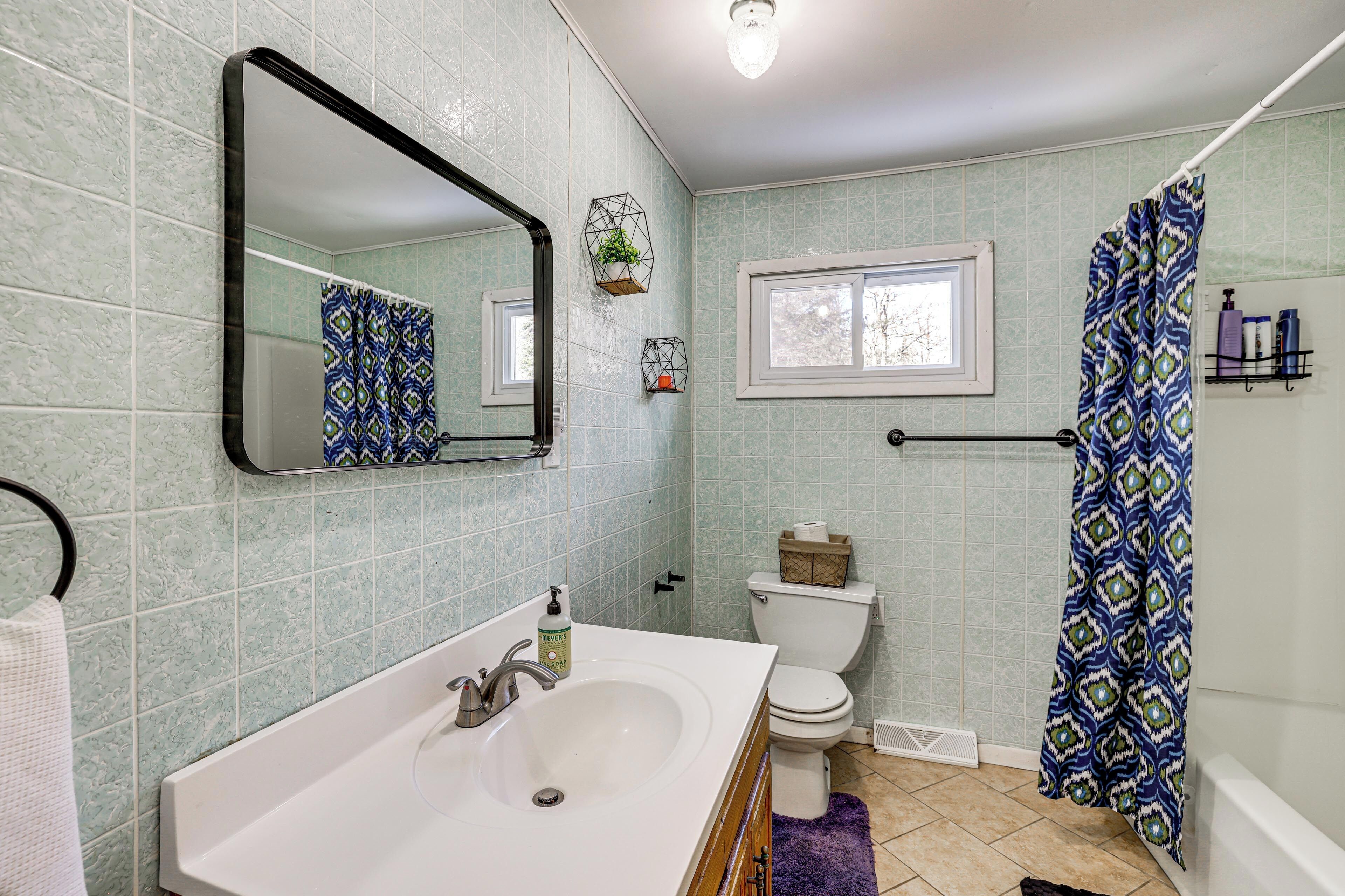 A bathroom with a white sink, a toilet, a shower curtain, and a window.
