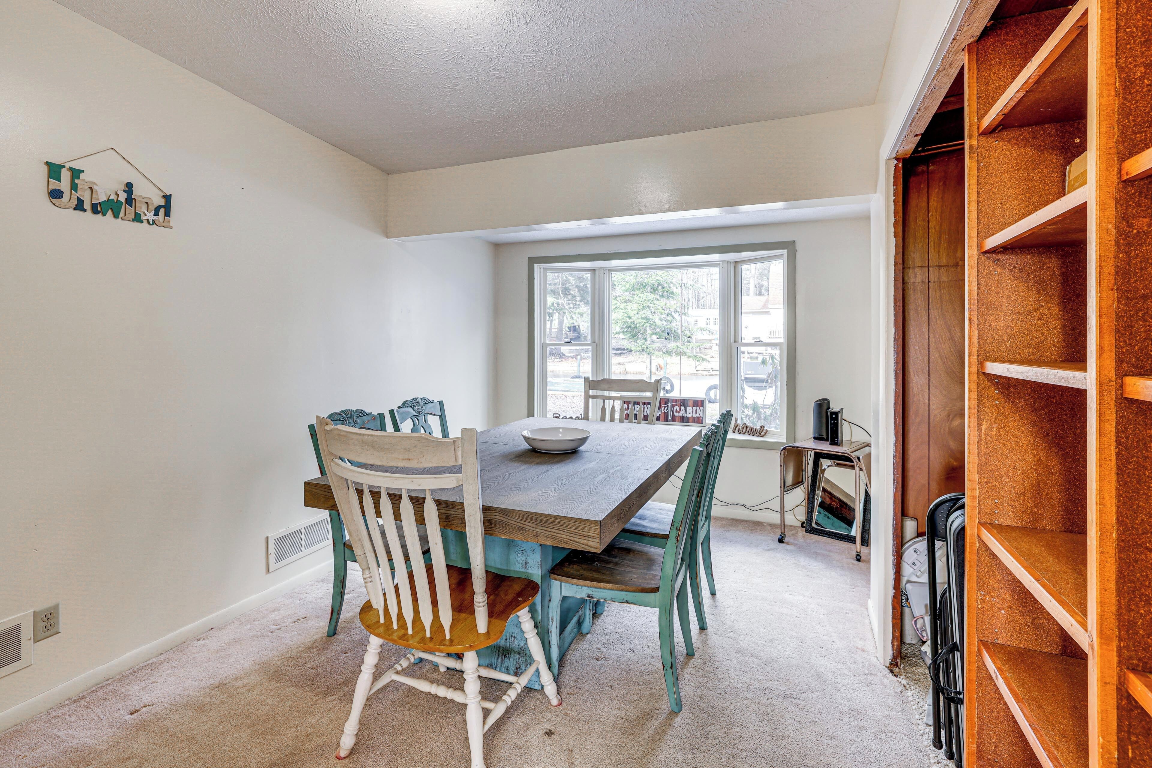 A dining area with a wooden table and chairs, a window with a view, and a bookshelf.