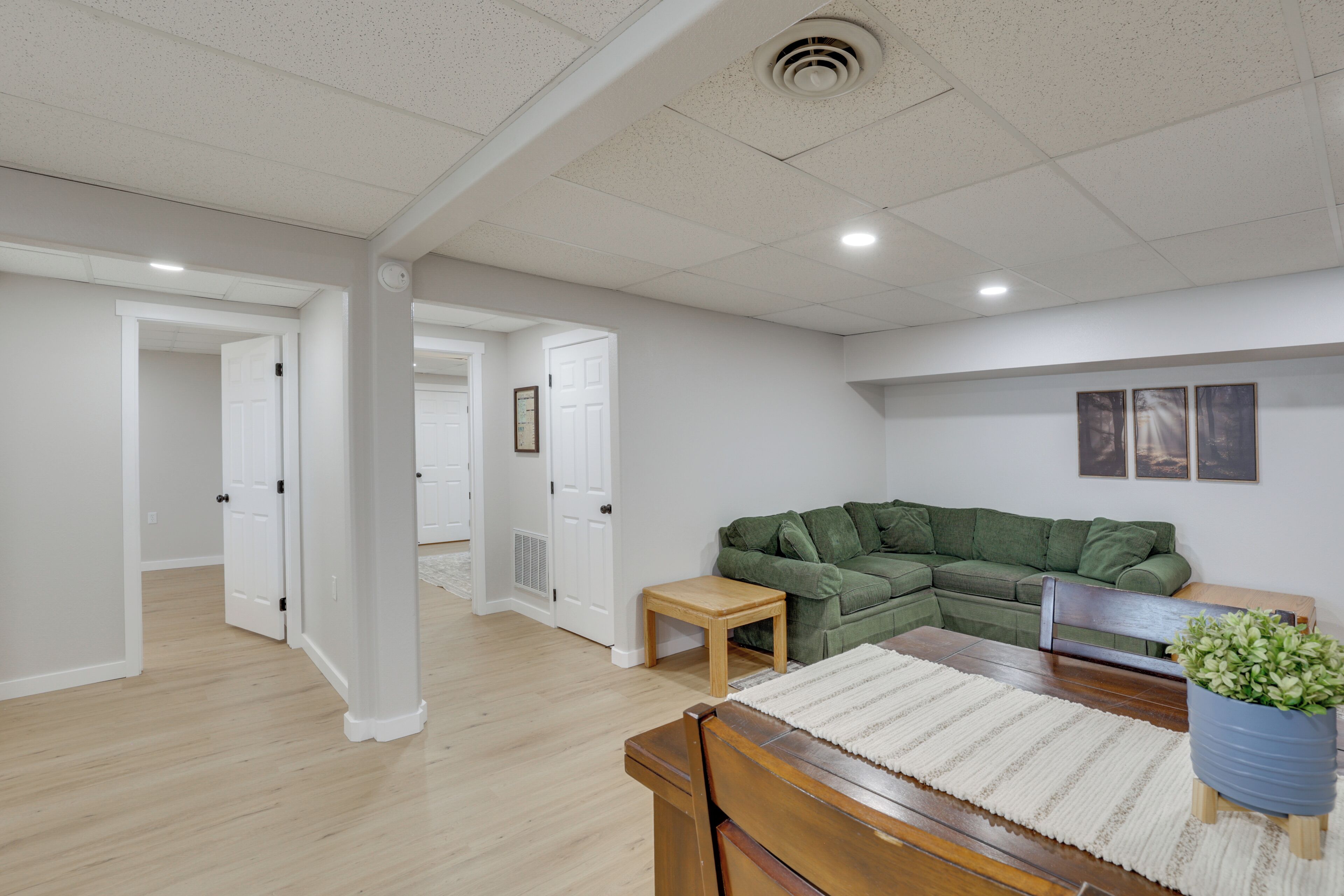 A spacious living room with a wooden dining table, a green sectional sofa, and a small wooden side table.