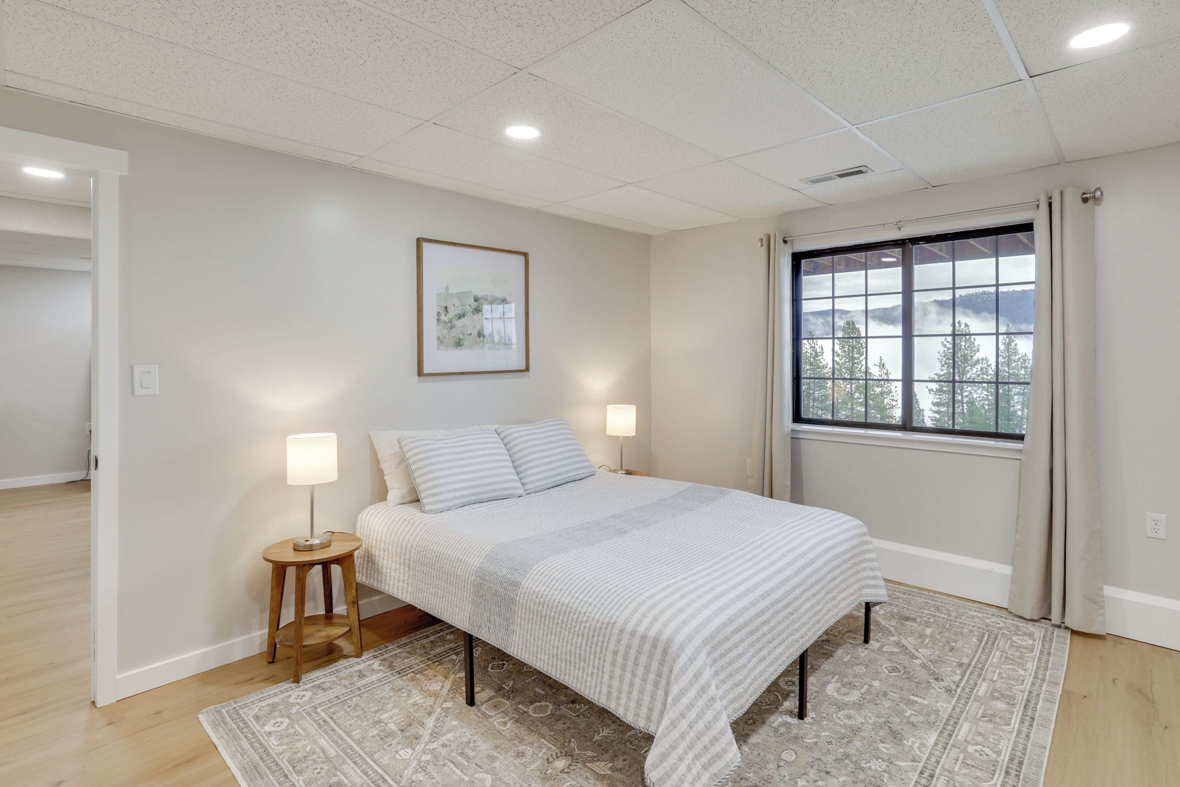 Quarto com cama, abajures, janela com vista e porta para outro cômodo.