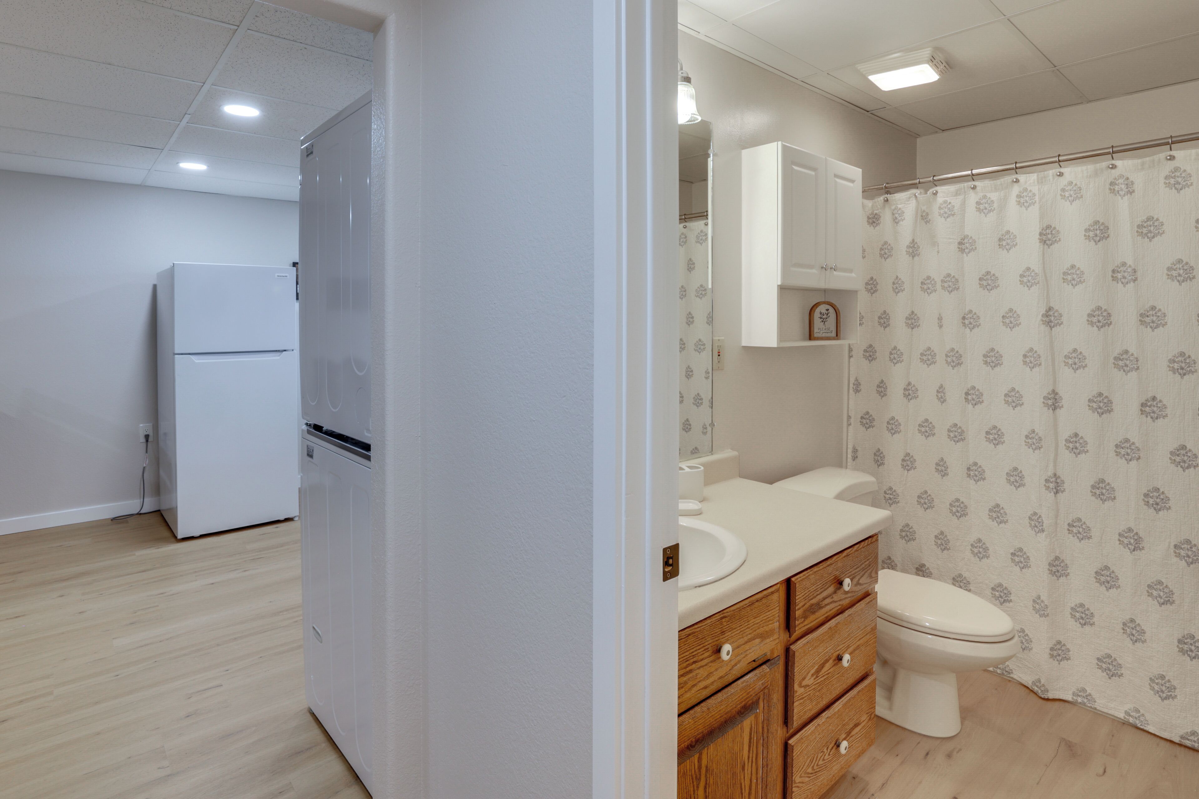 Un baño con inodoro, lavamanos y un armario, además de una zona de ducha con cortina estampada.
