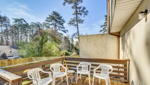 Una terraza de madera con sillas de plástico y una pequeña mesa, con vista a una zona boscosa.