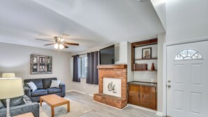 Una sala de estar con sofá, mesa de centro, chimenea, ventilador de techo y puerta con ventana.