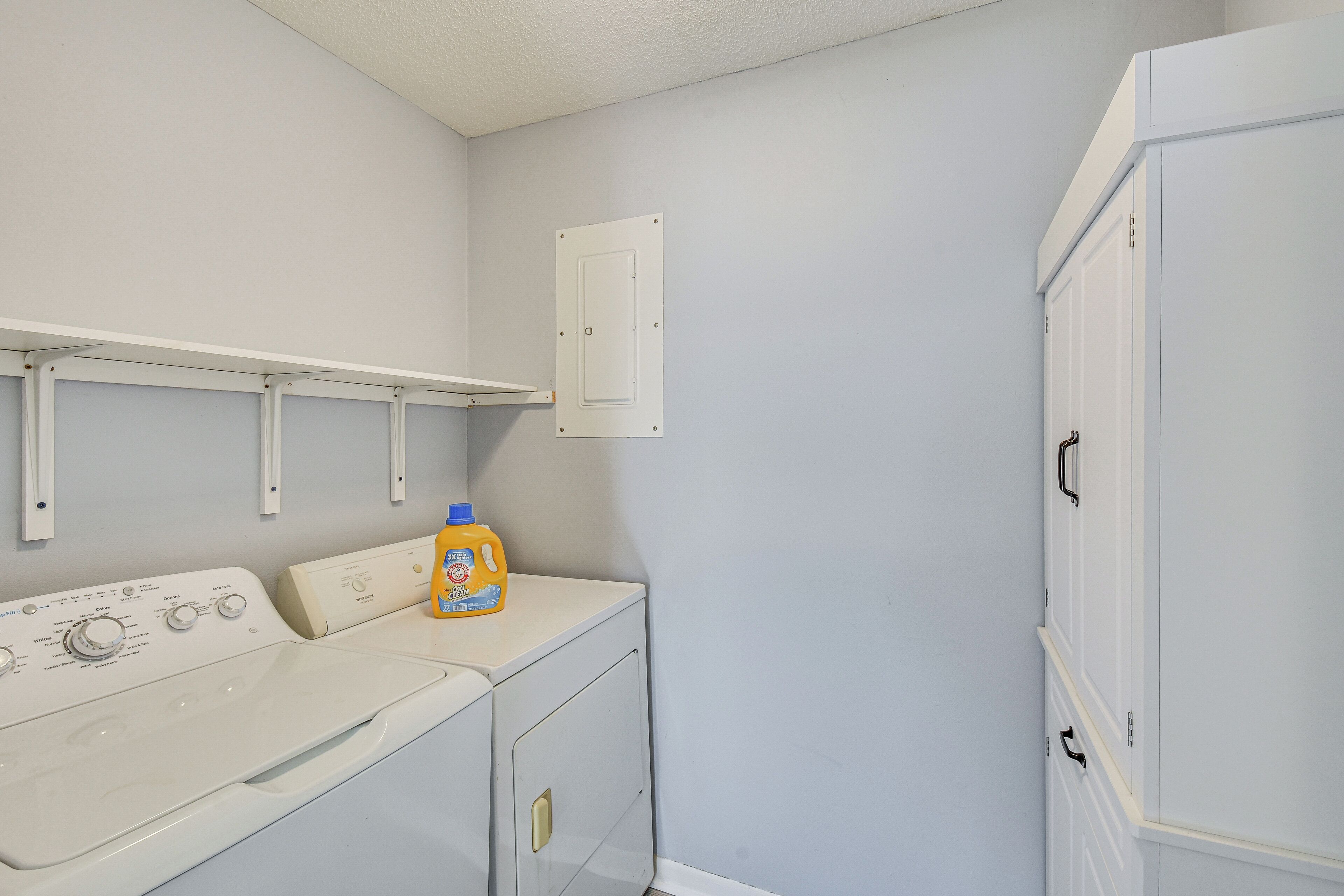 A laundry area with a washing machine, a dryer, and a cabinet with a detergent bottle.