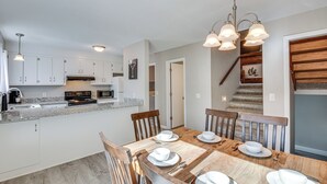 Una cocina moderna con armarios blancos, encimera de granito y comedor con mesa de madera dispuesta para cuatro.